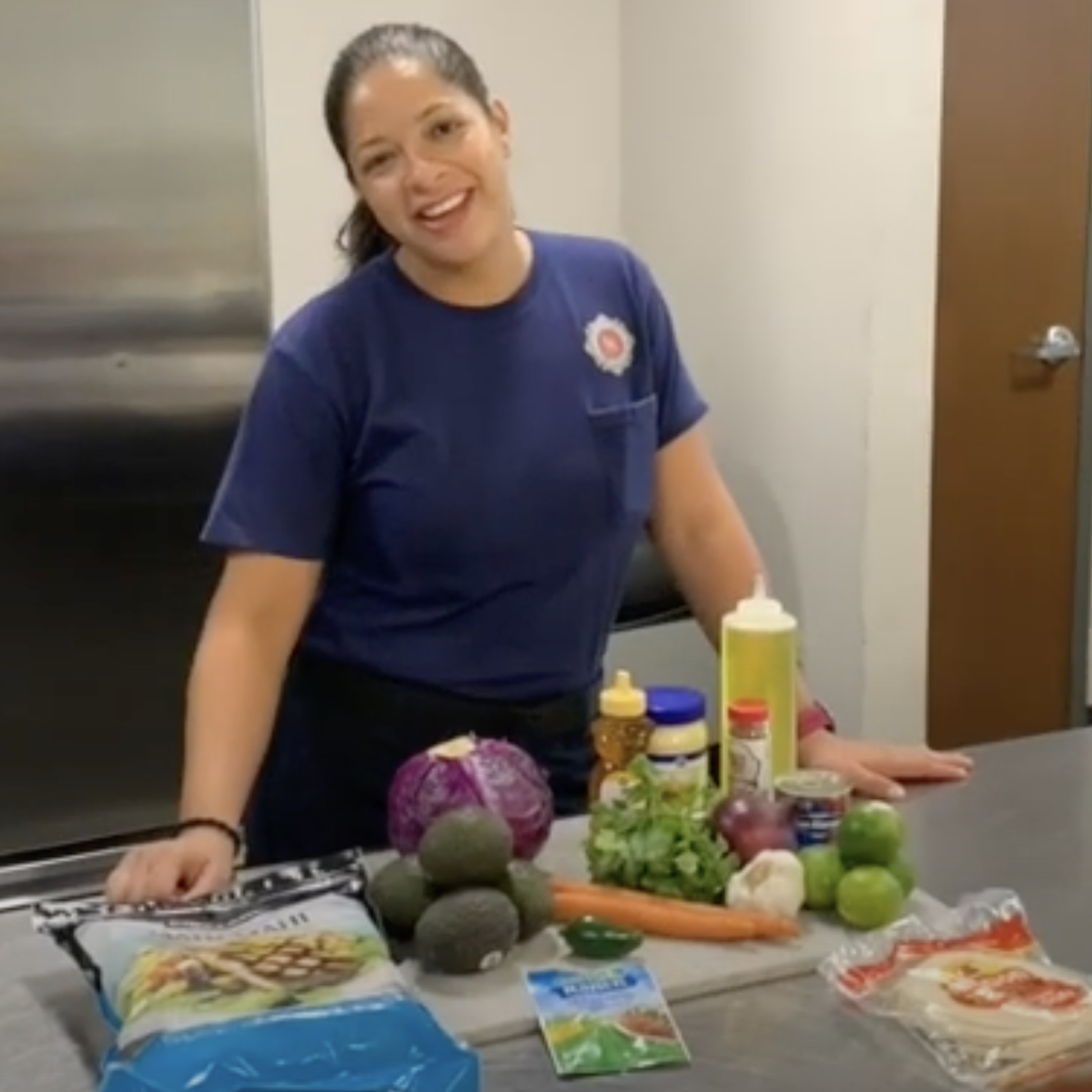 Lauderhill Fire Rescue Driving Engineer Melissa Vega stands at a stainless steel counter in a kitchen with various groceries and a cutting board.