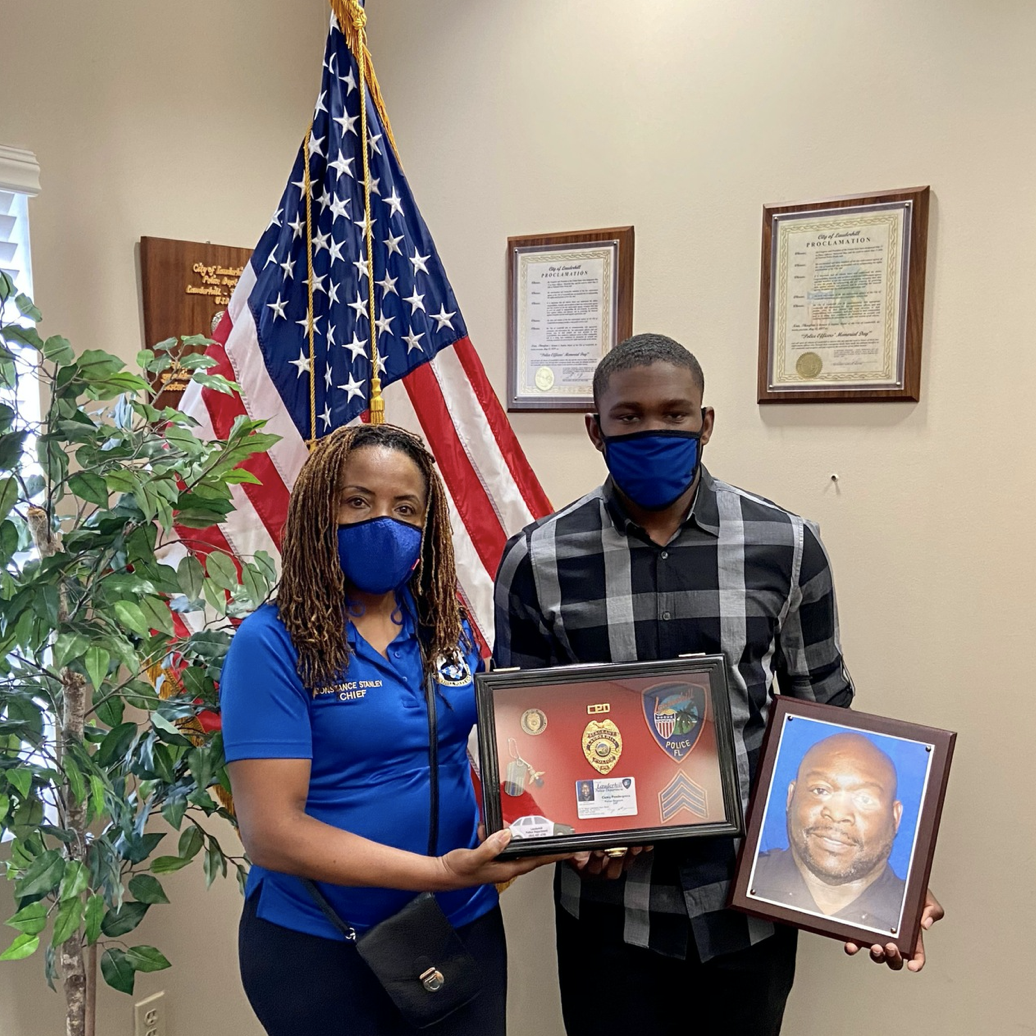 Chief Stanley with Cody Pendergrass inside office holding two frames