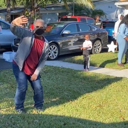 Mr Wilkerson in his front yard with people in the background by cars parked in a driveway