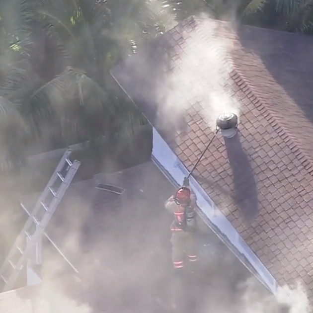 ladder and firefighter standing on roof tending to smoke emitting from chimney of a house