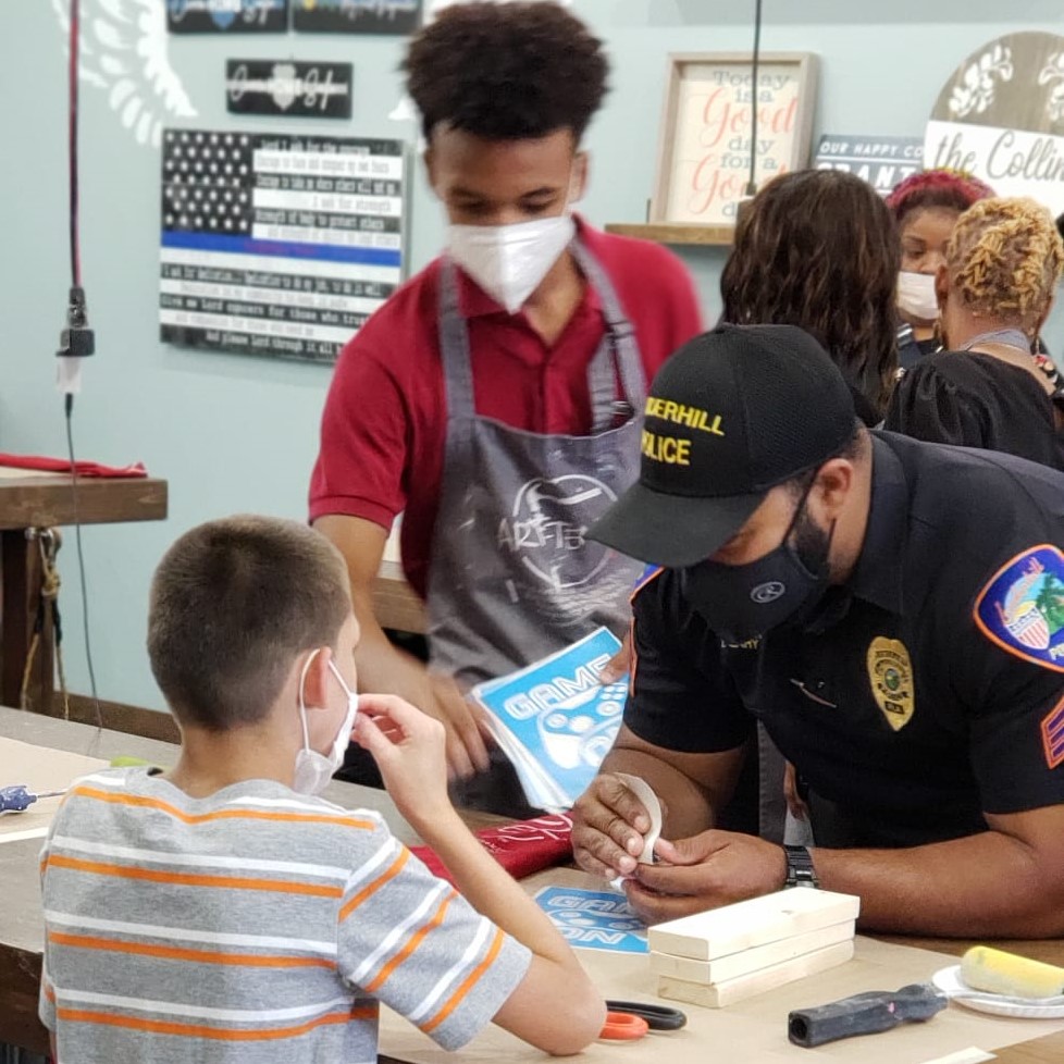 Lauderhill police officers and students with autism work on crafts on either side of a long table indoors