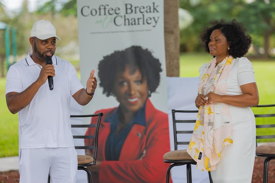 commissioner s ray martin speaking into microphone on an elevated stage outdoors beside vice mayor denise d grant