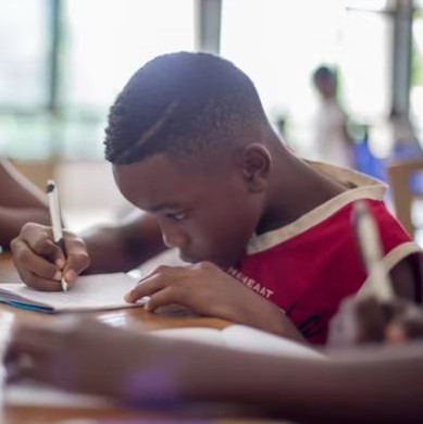 School age boy writing on notepad onto shared desk